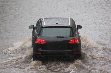 Modern siyah araba, bir bahar günü, şehrin bir caddesinde, derin yağmur altında derin bir su birikintisinin içinden geçer, motor hidrolik şok tehlikesi, dikiz aynası