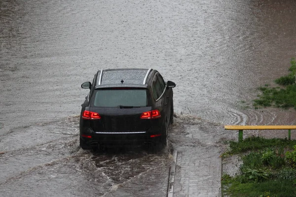 春の日に公園の道路上の大雨の中 新しい黒いSuv車は慎重に深い水たまりに入ります バックビュー — ストック写真