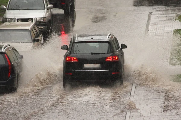 黒のドイツの高級Suv車は 春の日に街の大雨の中で駐車車の横に重いスプレーで高速運転 バックビュー — ストック写真