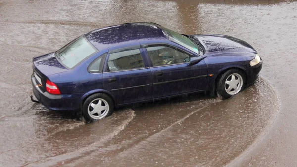 濃い青のセダン車を慎重に大規模な水たまりを介して 街の大雨に乗る — ストック写真