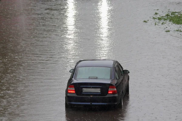 一辆黑色的汽车驶过了一个大水坑 车前的车灯反射着 城里下着大雨 — 图库照片