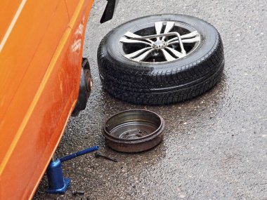 Silinmiş tekerlek ve fren trampeti yolda, arabanın yanında hidrolik krikonun üzerinde duruyor, tamirat yolda.