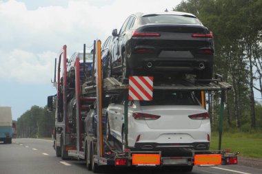 İki katlı, iki eksenli araba taşıyıcı tırı olan iki katlı kamyon banliyö otobanında yeni arabalar taşıyor, arka taraf görüntüsü yakın, otomobil teslimatı var.