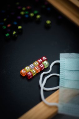 Siyah arkaplan ve yüz maskesi üzerine renkli kelime CORONA VIRUS İngiliz alfabe küpü, seçici odaklanma