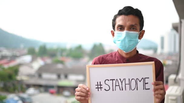 医療用マスクの若いアジア人男性 カメラを見て 図面を表示 Stayhome 病気やほこりを防ぐために 午後5時 家庭用検疫コロナウイルスパンデミック予防に滞在 スペースのコピー — ストック動画