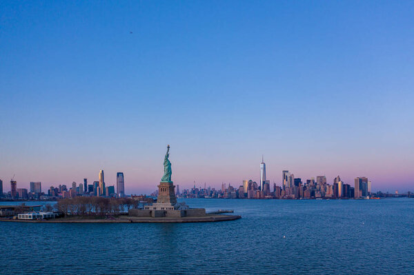 Statue of Liberty and New York Manhattan cityscape in background at sunset, USA