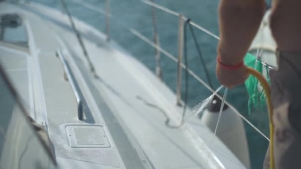 En mann vasker en yacht med en slange med vann i sakte bevegelse – stockvideo