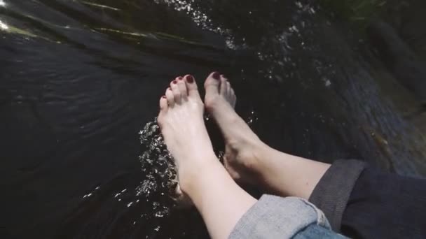 Женщина, сидящая у реки на краю скалы — стоковое видео