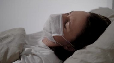 Tıbbi maskeli hasta kadın öksürüyor. Hastane odasında, yüzü kapalı bir şekilde yatıyor.