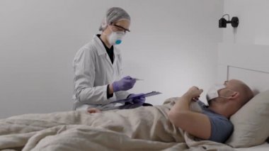 Yüzünde koruyucu solunum cihazı olan doktor grip olan erkek hastayı muayene ediyor.