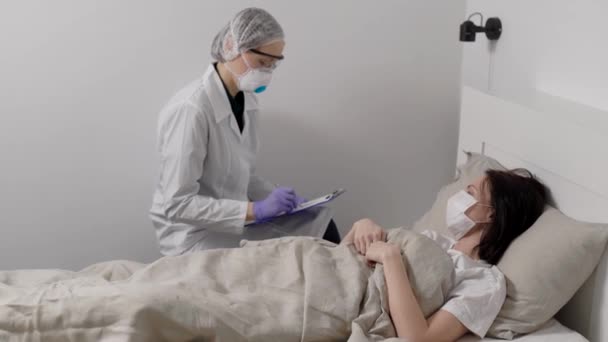 Lekarz wirusolog pyta pacjentkę z nieznanymi chorobami w pokoju szpitalnym, wypełniając papier — Wideo stockowe