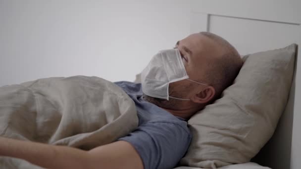 Grippekranker erwachsener Mann liegt mit medizinischer Maske auf Mund und Nase im Bett und hustet — Stockvideo