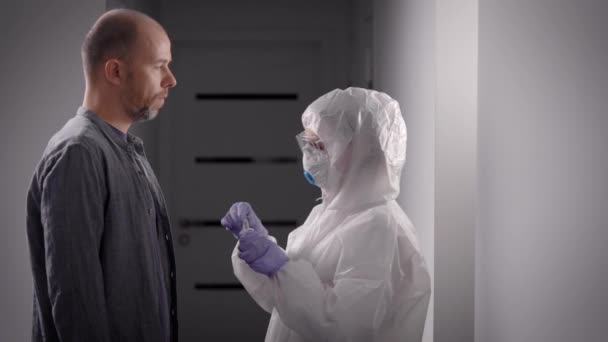 Пандемия Ковид-19. Врач в защитном костюме проходит тест у пациента дома. Вирусный тест — стоковое видео