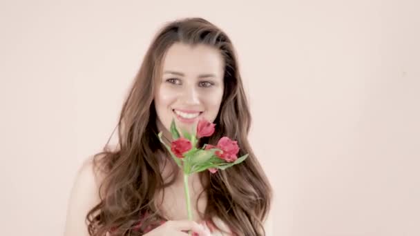 Молода красива жінка з коричневим довгим хвилястим волоссям тримає червону квітку в руках, м'яко посміхається, грайливо обертається — стокове відео