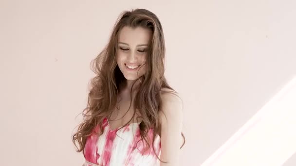 Mujer atractiva joven modelo de moda con pelo largo y castaño con sonrisas de maquillaje y bailes sobre un fondo claro — Vídeos de Stock