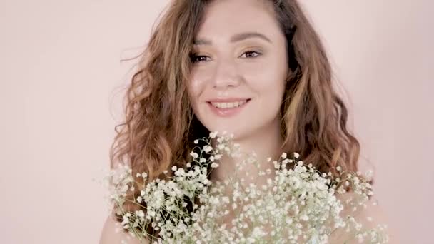 Retrato de una joven hermosa mujer sonriente con maquillaje con una larga mujer de pelo rizado marrón sosteniendo un ramo de flores blancas — Vídeos de Stock