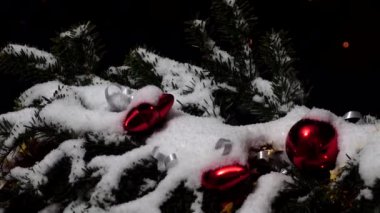 Noel ağacının dalları karların altında oyuncaklarla süslenmiş. Gece bir şehrin arka planında çekim yapmak.