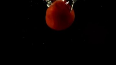 Domatesin suya düşmesi. Ağır çekim. Siyah arkaplan.