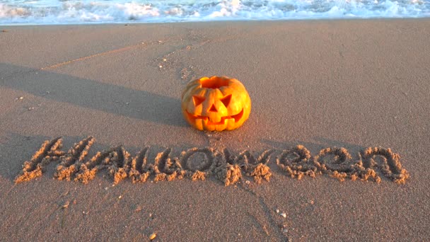 Strašidelná halloweenská dýně. Inscription Halloween na písku mořské pláže. Moře a vlny. Natáčení v říjnu.
