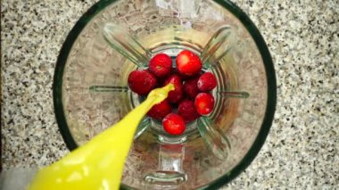 Portakal suyu çilekli blender kasesinde akar. Ağır çekim. Mutfakta çekim. Üst görünüm.