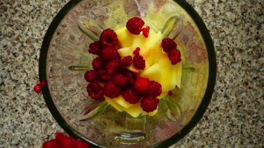 Ahududu elma parçalarının üzerine blender kasesine düşer. Ağır çekim. Mutfakta çekim. Üst görünüm.