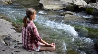 Kız dağ nehri taşları üzerinde yoga yapıyor. Yazın çekim..