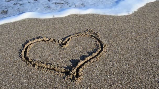 A rajzoló szív a homokon. A szívet elmossa egy tengeri hullám. Lövöldözés a parton.