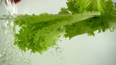 Marul yaprakları ve kiraz domatesleri suya düşer. Yavaş çekim.