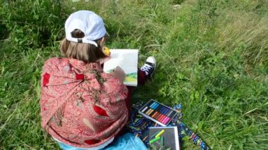 Kız hayattan bir dağ manzarası çiziyor. Çizim bir pastel boya ile yapılır..