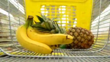 Süpermarketteki el arabası. Muz ve ananas sepete konur. Arabanın hareketi, ürün seçimi..
