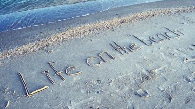 Sahilde çekim yapmak. Sahilde yaşam kavramı. Sahilde bir kumsalda gelen dalgalarla yazılmış yazı.