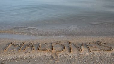 Maldivler kumun üzerindeki yazıyı gösteriyor. Kumsalda, kumsalda..