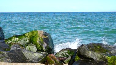 Deniz dalgaları taşlara çarpıyor. Deniz kıyısında ateş ediyorlar. Yavaş çekim.