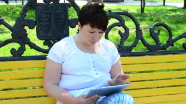 Tabletli bankta oturan kız. Park halindeki kız tabletle çalışıyor.