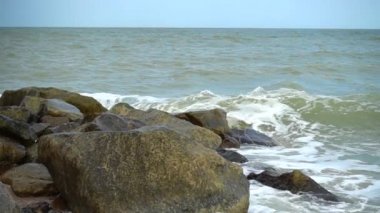 Deniz dalgaları taşlara çarpıyor. Deniz kıyısında ateş ediyorlar. Yavaş çekim.