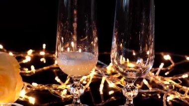Şampanya kadehleri ve parlak çelenklerin arkasında bir gül..