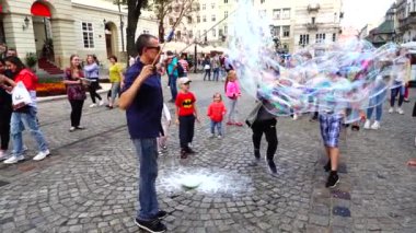 LVIV, UKRAINE - 3 AĞUSTOS 2019: Bilinmeyen adam, çocuklar için sabun köpüklerinin şehrin meydanlarına çıkmasına izin veriyor. Yavaş çekim.