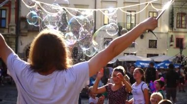 LVIV, UKRAINE - 25 Ağustos 2019: Bilinmeyen bir adam şehir meydanında sabun köpüklü çocukları eğlendiriyor. Yavaş çekim.