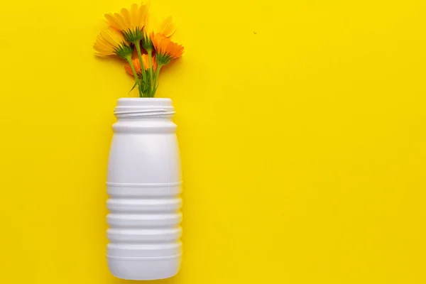 Reused white plastic bottle with flowers on a yellow background located on the left. Plastic recycling to yellow container