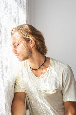 Orta boylu, sarı saçlı, evden çıkamadığı için hayal kırıklığına uğramış genç bir adam. Yalnızlık ve sessizlik kavramı. Pencereden eve güneş ışınları geliyor..