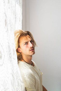 Orta boylu, sarı saçlı, evden çıkamadığı için hayal kırıklığına uğramış genç bir adam. Yalnızlık ve sessizlik kavramı. Pencereden eve güneş ışınları geliyor..