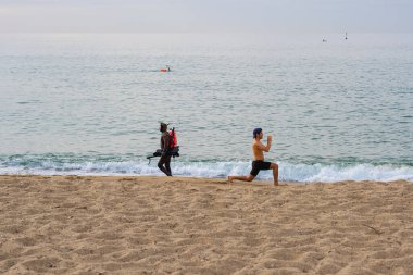 BARCELONA, İspanya - 25 Mayıs 2020: Barcelona 'da Coronavirus hastalığının (COVID-19) birinci safhasının ilk günü, bir sualtı balıkçısı ve plajda spor yapan genç bir adam