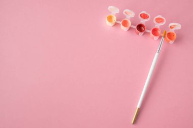 Düz yatıyordu, masanın üst görüntüsü. Pembe arka planda küçük bir kavanozda resim yapmak için sanatçı fırçası ve boya.