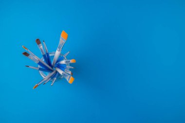 Flay lay lay, üst görünüm masa. Mavi arka planda cam bir stantta farklı sanatçılar fırçalar.