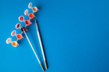 Düz yatıyordu, masanın üst görüntüsü. Mavi arka planda küçük bankalarda çizim yapmak için farklı sanatçı fırçaları ve çok renkli boyalar.