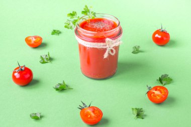 Bardak kavanozunda maydanoz yapraklı domates suyu ve taze domates. Açık yeşil arkaplan