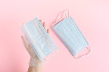 Koruyucu eldivendeki üstteki el, virüslere karşı tıbbi bir maske ve pembe arka plandaki bakterilere karşı koruyucu tıbbi bir araç tutuyor..