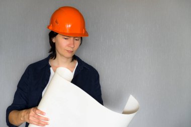 Gri arkaplanla ilgili planlara bakan güzel bir mimar kadın. İş yerinde ciddi bir kadın. Boşluğu kopyala.