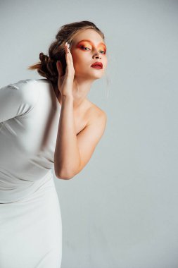 Beyaz elbiseli güzel bir kız, beyaz bir arka planda, makyaj yapıyor, güzel duygusal pozlar veriyor.