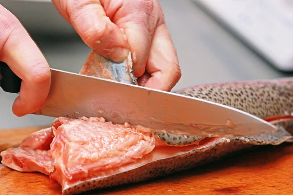 cook carving red fish on the board with a knife, prepare sushi, horizontal, background, blurry
